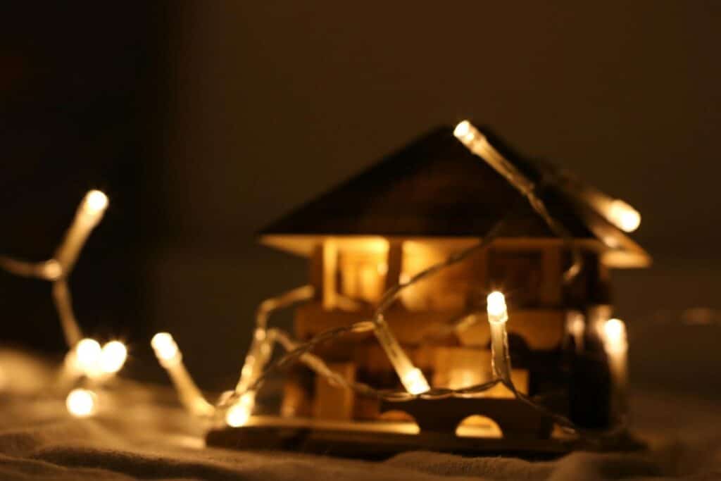 A miniature wooden house beautifully illuminated by warm white Christmas string lights.