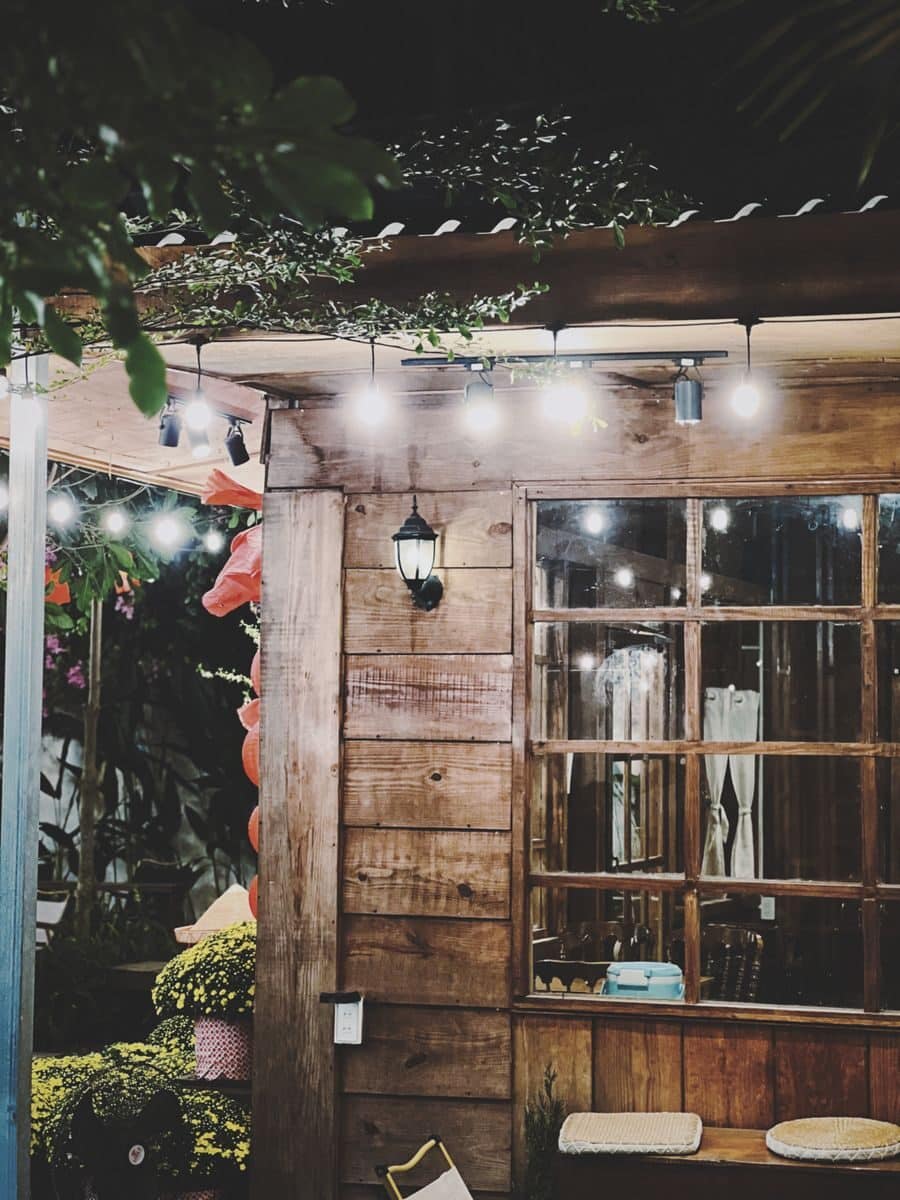 A charming rustic cafe exterior with wooden walls and string lights creating a warm ambiance at night.