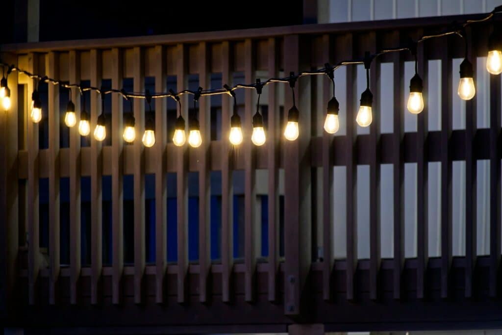 String lights illuminate a wooden deck railing at night.